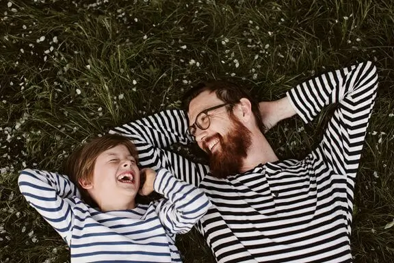 father and son in striped tops laying on grass with their hands behind their heads relaxing